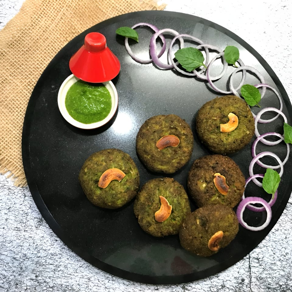 Six green patties topped with cashews, served with green chutney, onion rings, and mint.