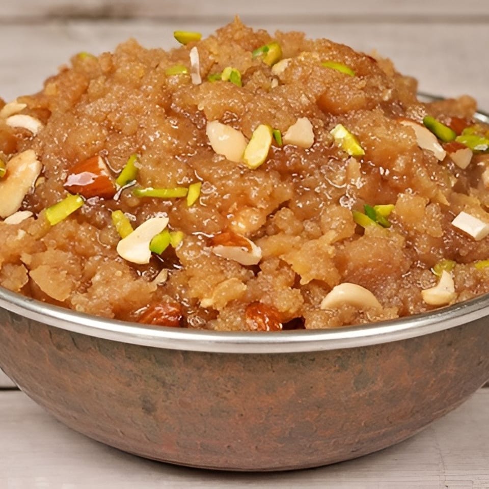 A copper bowl filled with halwa, garnished with slivered almonds, cashews, and pistachios.