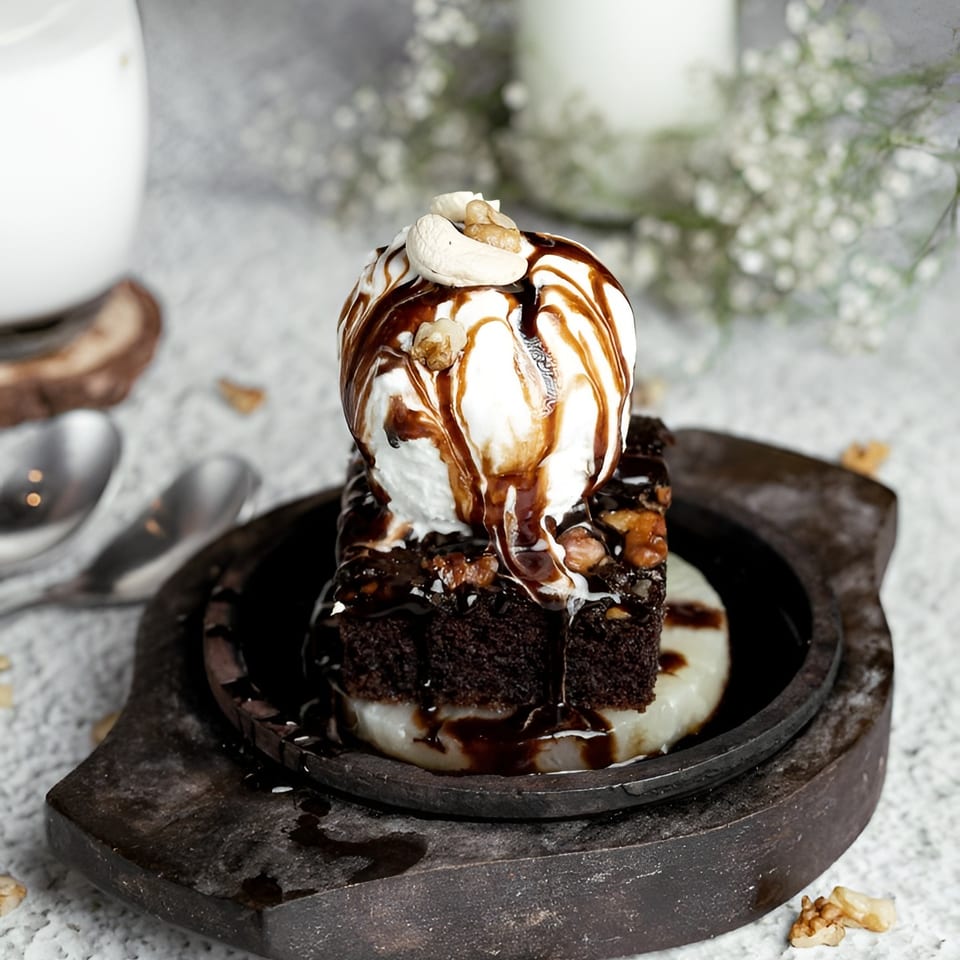 Chocolate brownie with vanilla ice cream, chocolate syrup, and nuts on a sizzling plate.
