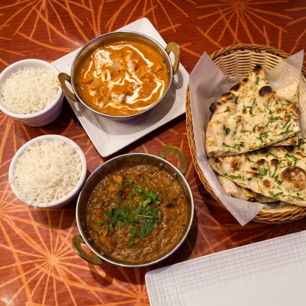 Indian meal with two curries, basmati rice, and naan bread on a patterned orange table.