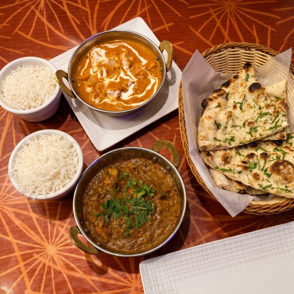 Indian meal with two curries, basmati rice, and naan bread on a patterned orange table.